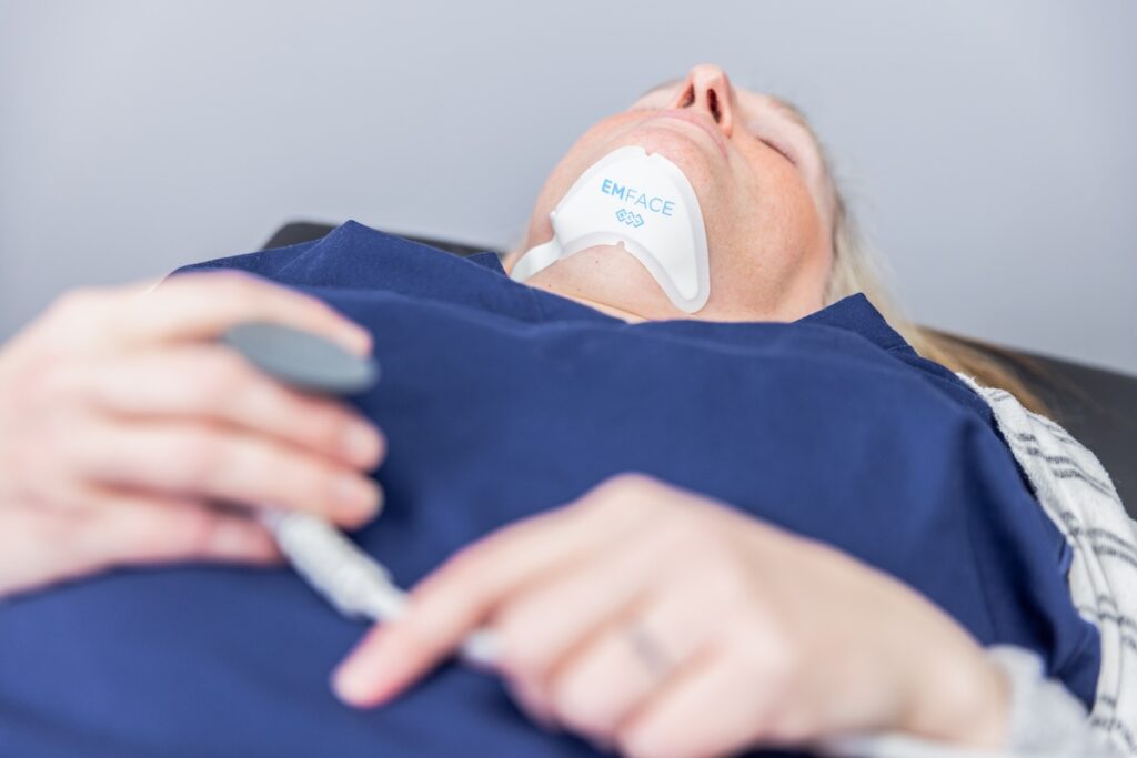 A patient lies back with the Emface Submentum applicator under the chin during their nonsurgical facelift in Elgin.